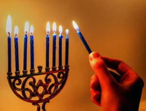 Hand Lightting start of david Chanukah Menorah with blue candles and gold background
